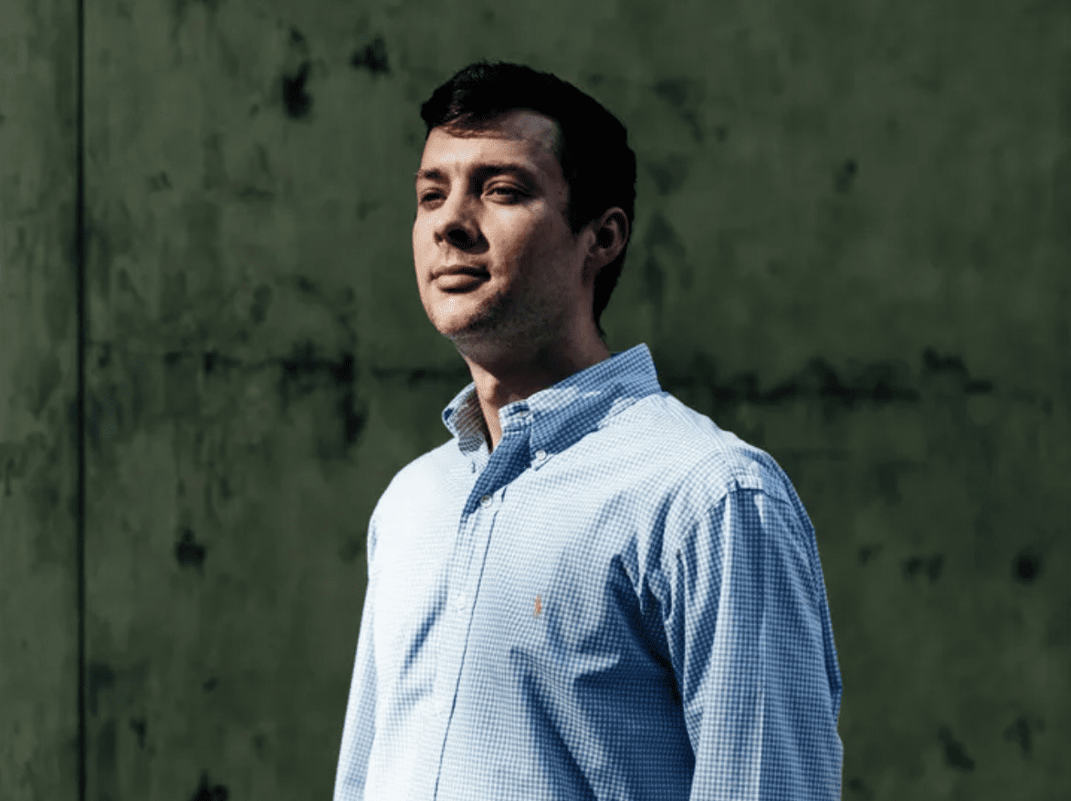 A man in a blue shirt standing next to a wall.