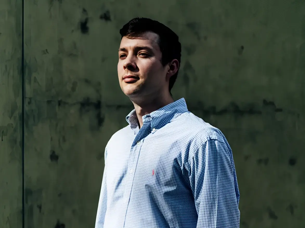 A man in a blue shirt standing next to a wall.