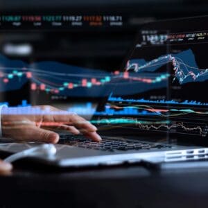 A person is typing on a laptop with a bunch of graphs in the background.