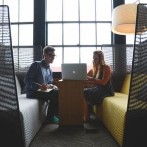Two people having a discussion in a cozy office booth with a laptop.