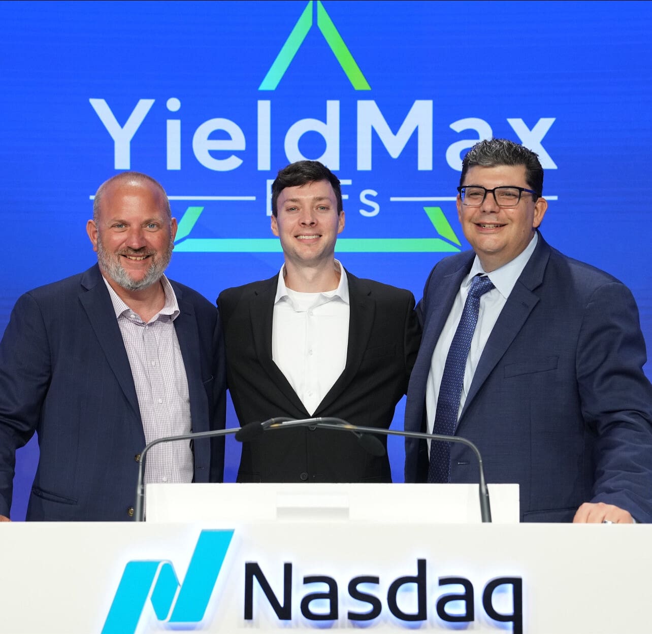 Three men standing behind a Nasdaq podium at an event.