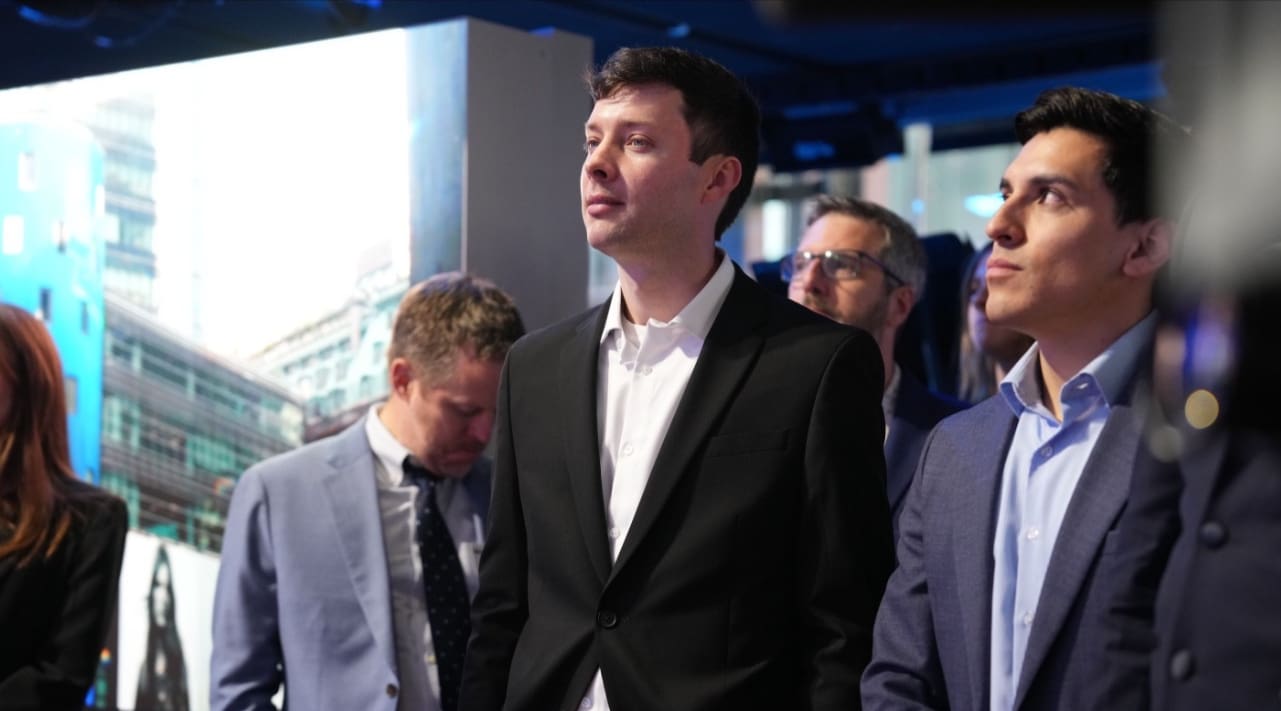 Young man in a black suit standing among a crowd at an event.