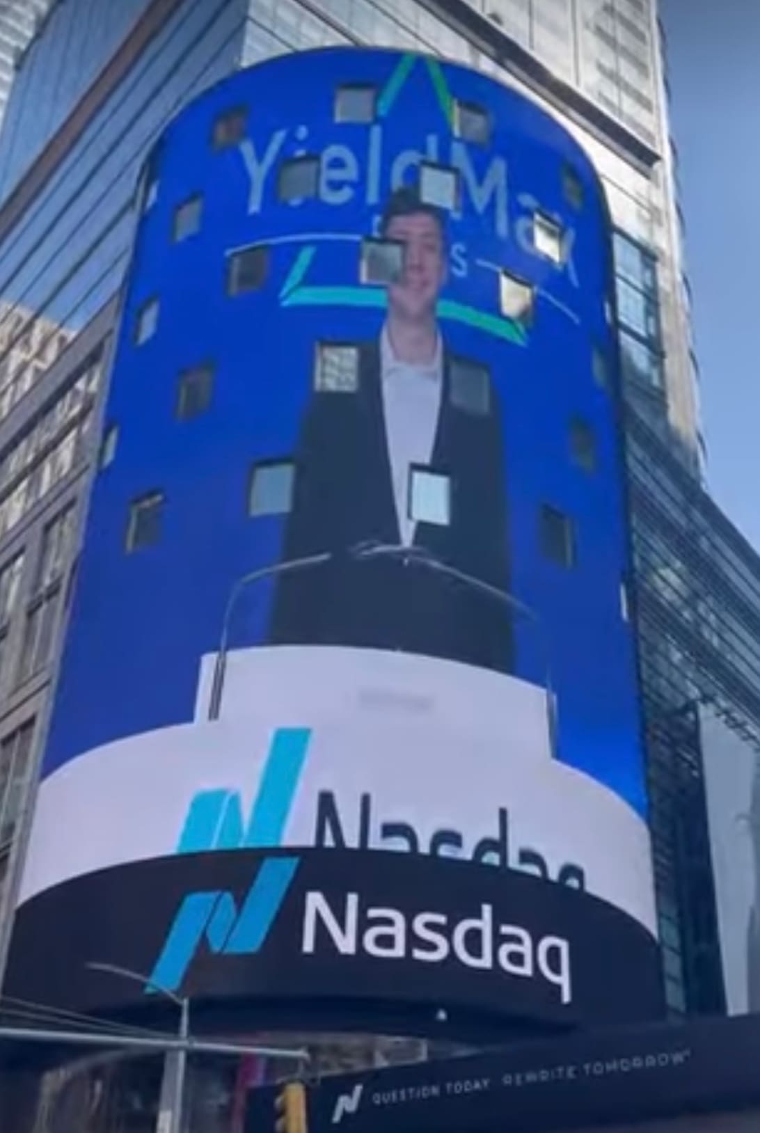 Person standing in front of a large Nasdaq digital billboard in a city.